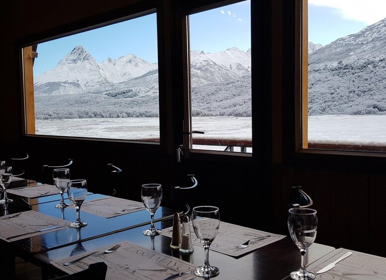 A dining table with wine glasses and menus, overlooking a snowy mountain landscape through large windows. 4