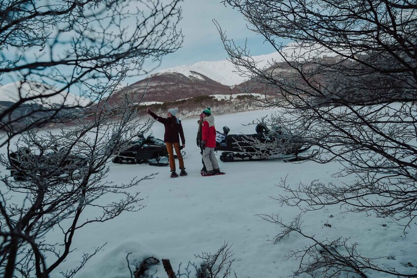 Two people standing in a snowy landscape with mountains in the background. 1