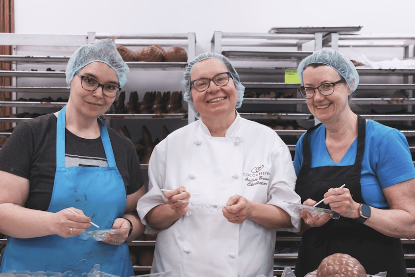 Three people in a bakery, wearing hairnets and aprons, handling dough and baking tools. 4