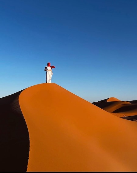 A person standing on a sand dune with a clear blue sky. 1