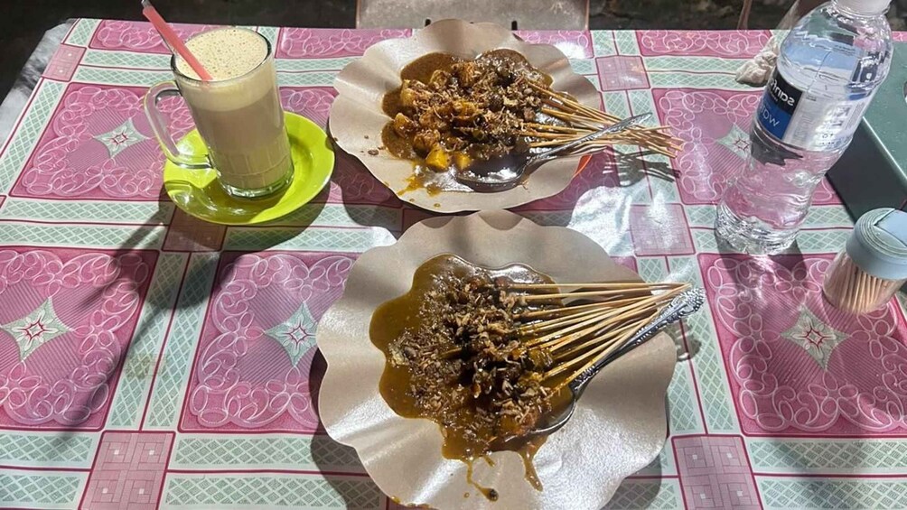 A table with a drink, skewers of grilled meat, and a water bottle. 4