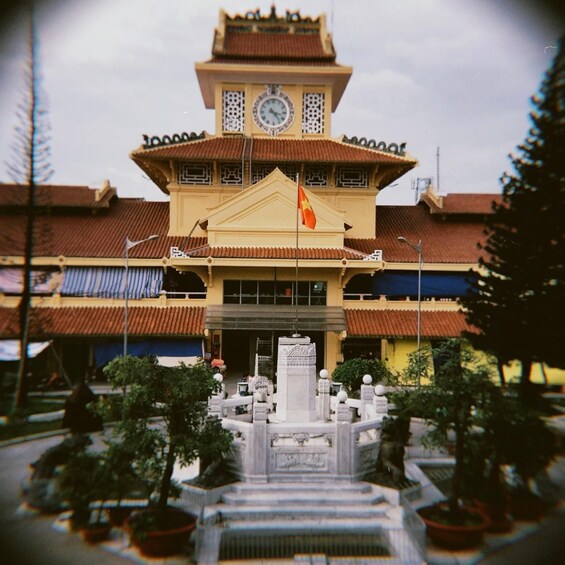 A traditional building with a clock tower, a flag, and a statue in front. 5