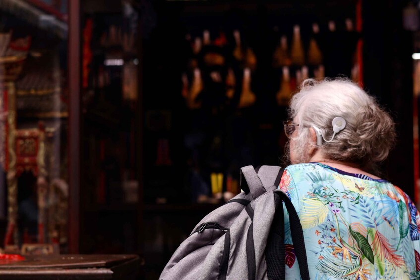 An elderly woman with a gray backpack, standing in front of a store with various items on display. 2