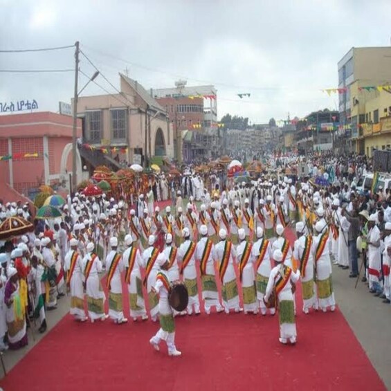 En gruppe mennesker i traditionelle dragter udfører en rituel dans på en rød løber i et bymiljø. 2