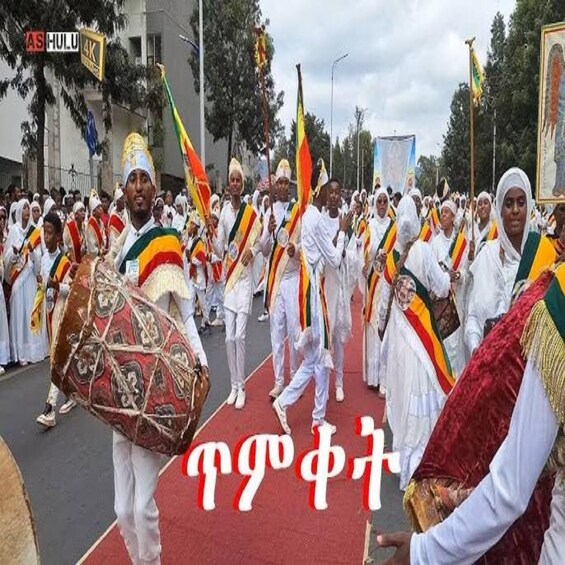 En gruppe mennesker i traditionelle dragter bærer flag og en tromme, mens de går på en rød løber. 3