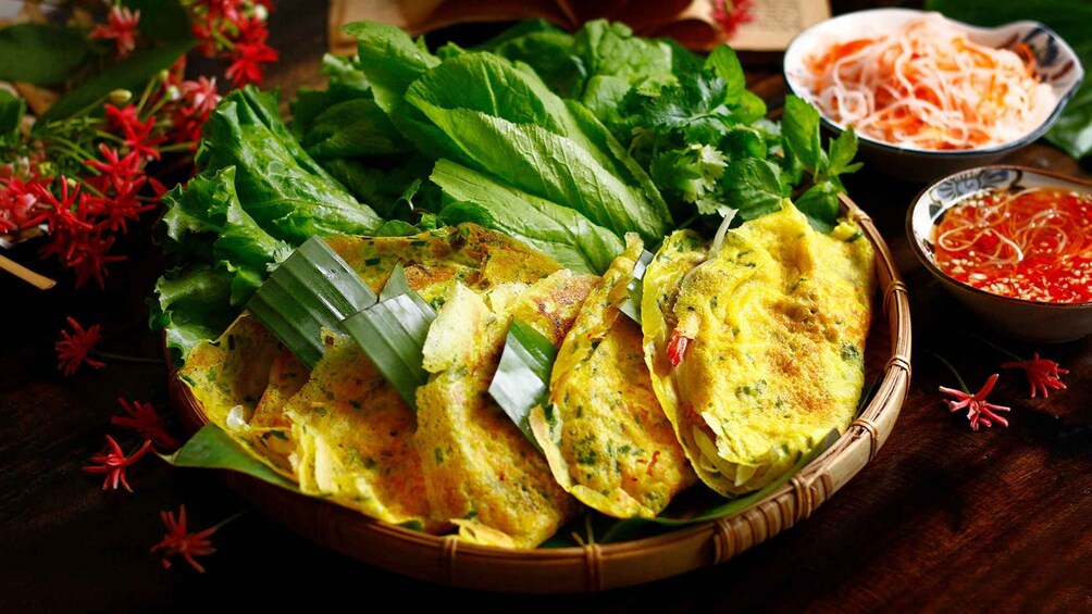 A basket of Vietnamese spring rolls with fresh herbs and a bowl of dipping sauce. 3