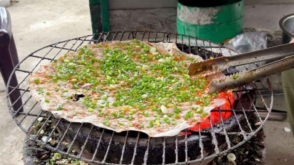 A flatbread being grilled on a metal grate with green onions and other toppings. 5