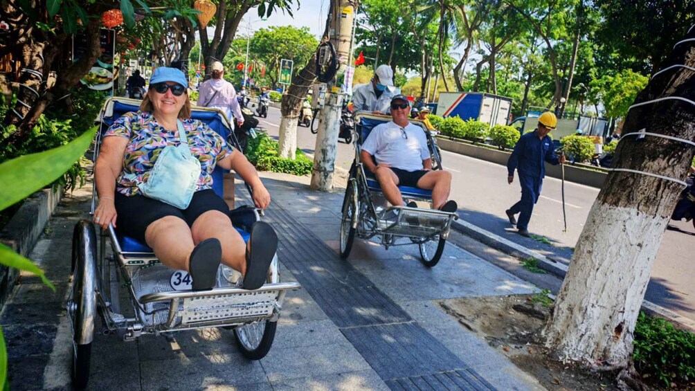 Two people in wheelchairs on a sidewalk with trees and a pedestrian in the background. 2