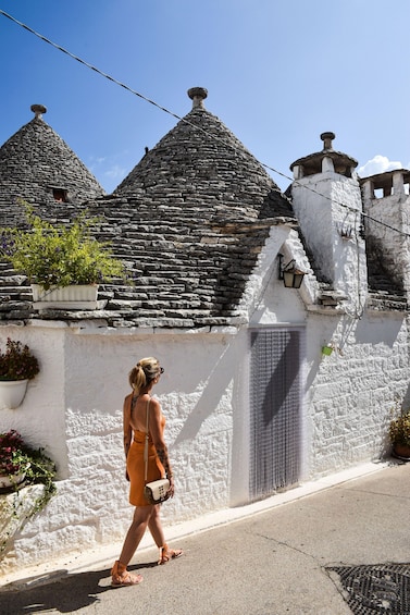A woman walking past a stone building with a white wall and a metal gate. 2