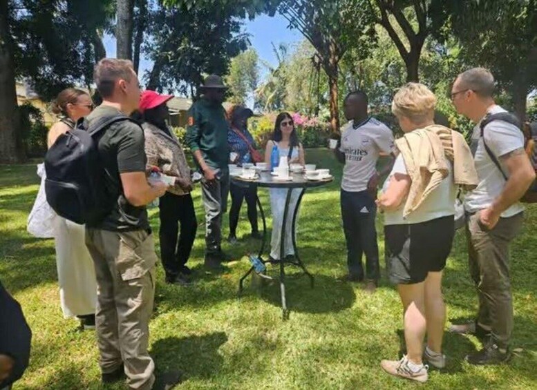 A group of people standing outdoors around a table with cups and saucers, suggesting a social gathering or event. 4