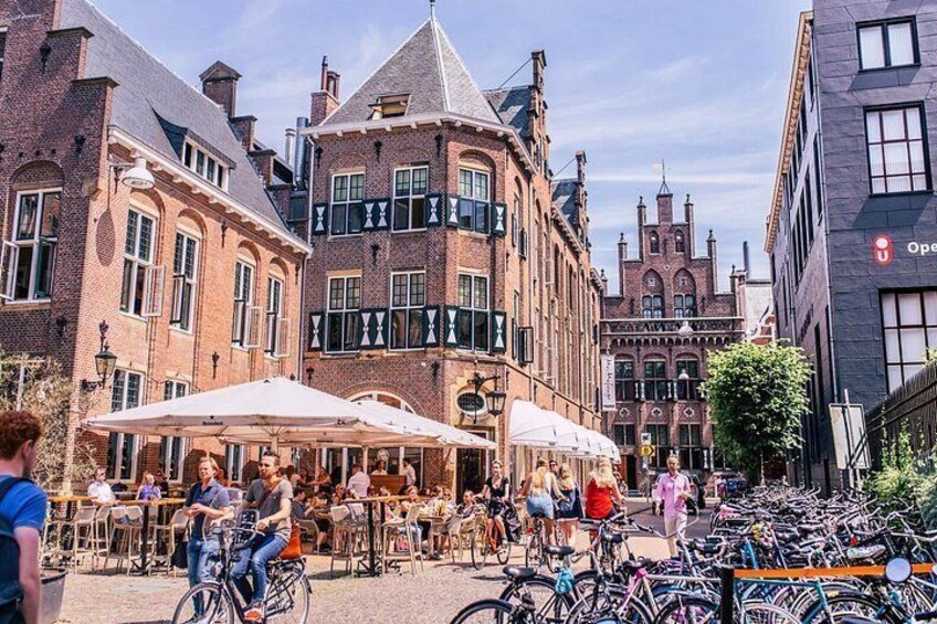 A bustling street with outdoor cafes, bicycles, and historic buildings. 1