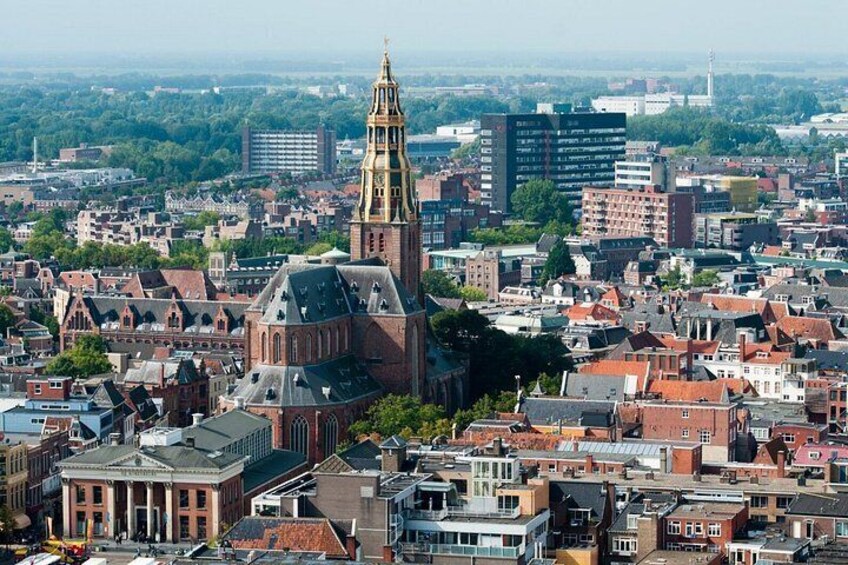 A cityscape with a prominent church featuring a tall spire, surrounded by dense urban buildings and greenery in the background. 2