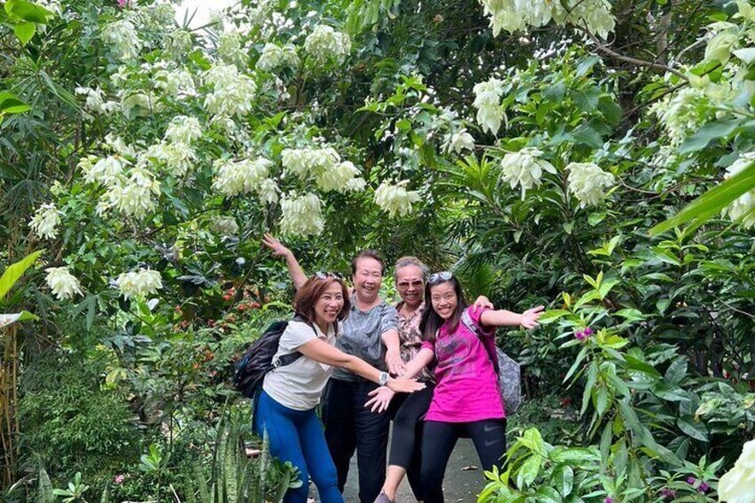 A group of people posing in a lush garden with dense foliage and white flowers. 2