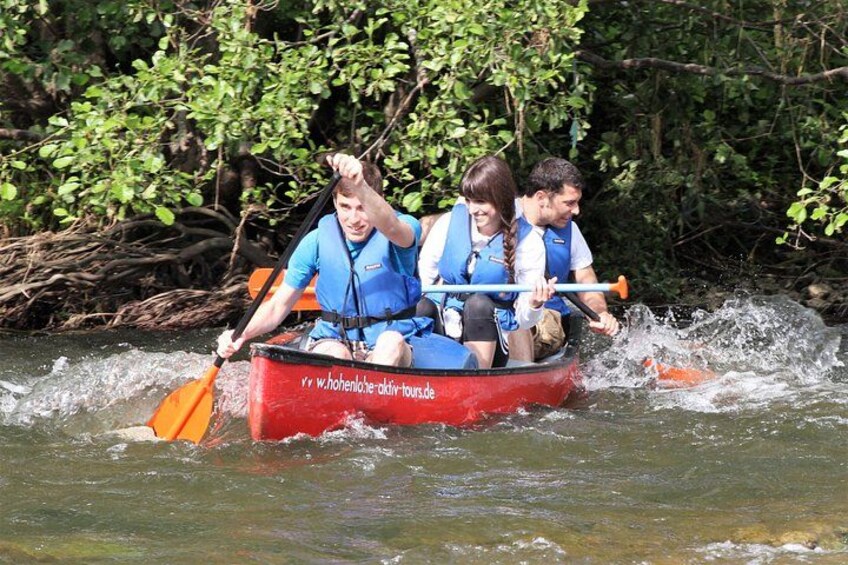 Three people in a red canoe on a river surrounded by greenery. 1