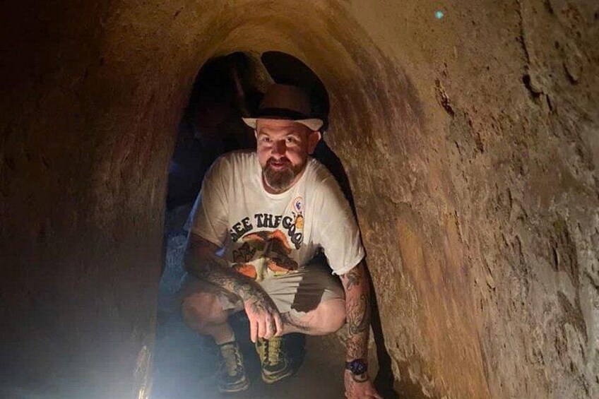 A person crouching inside a narrow, rocky tunnel. 4