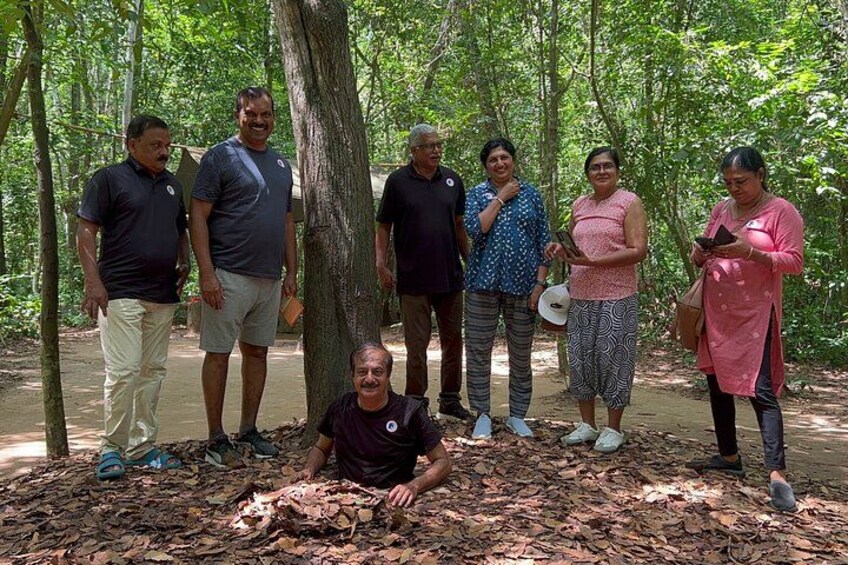 A group of people standing in a forested area with trees and leaf-covered ground. 4