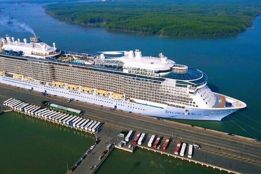 A large cruise ship docked at a port with multiple piers and smaller boats visible in the background. 1