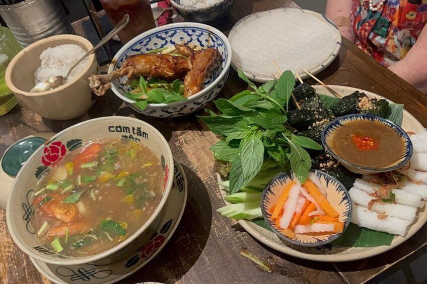 A table with various dishes including a bowl of soup, a plate of grilled chicken, and several small dishes with vegetables and dipping sauces. 2