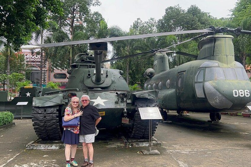 A military helicopter with the number 086, a couple standing in front of it, and a signboard. 3