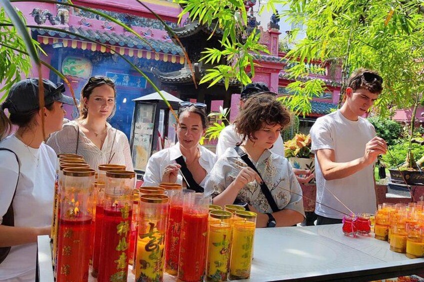 A group of people at a food stall with various drinks and a traditional building in the background. 3