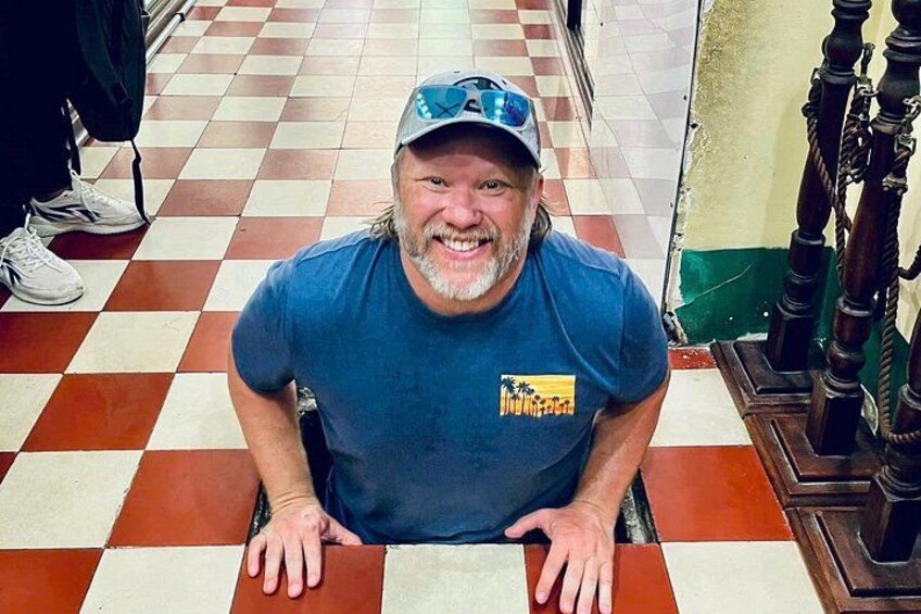 A person sitting on a tiled floor with a checkered pattern, wearing a blue t-shirt with a logo, and a cap. 2