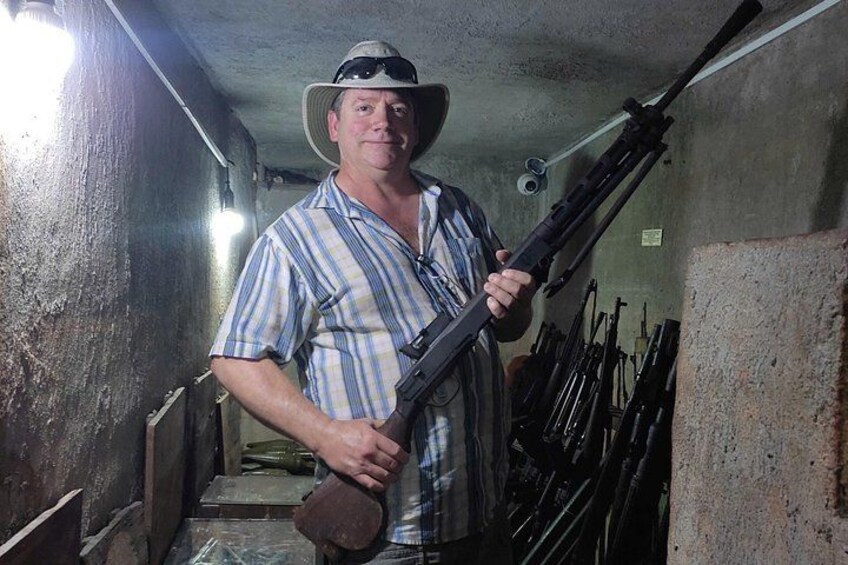 A man in a striped shirt and hat holding a rifle in a dimly lit tunnel with concrete walls and a metal railing. 5