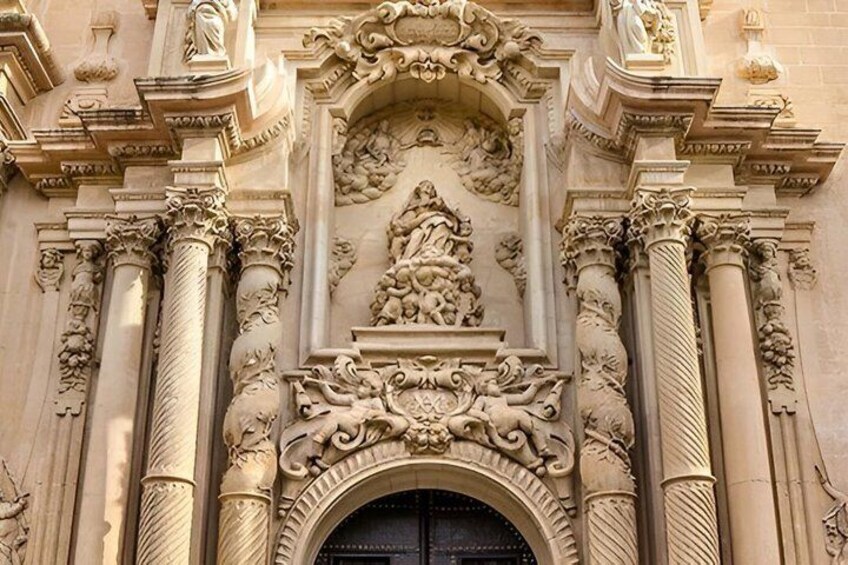 An ornate building facade with detailed carvings, columns, and a central archway. 1