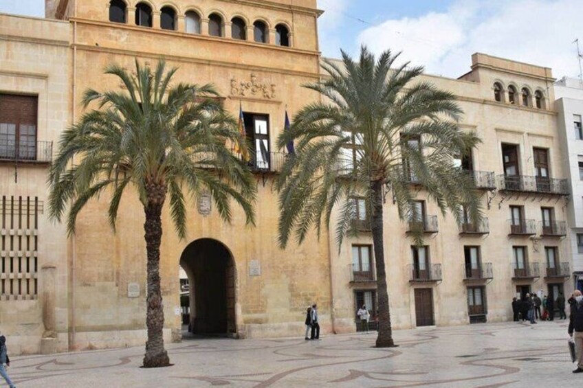 A historic building with palm trees in front, an arched entrance, and people walking around. 4