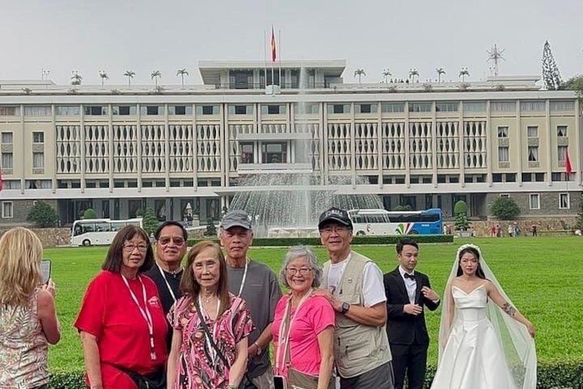 A group of people in front of a large building with a fountain, a bus, and a flag. 2