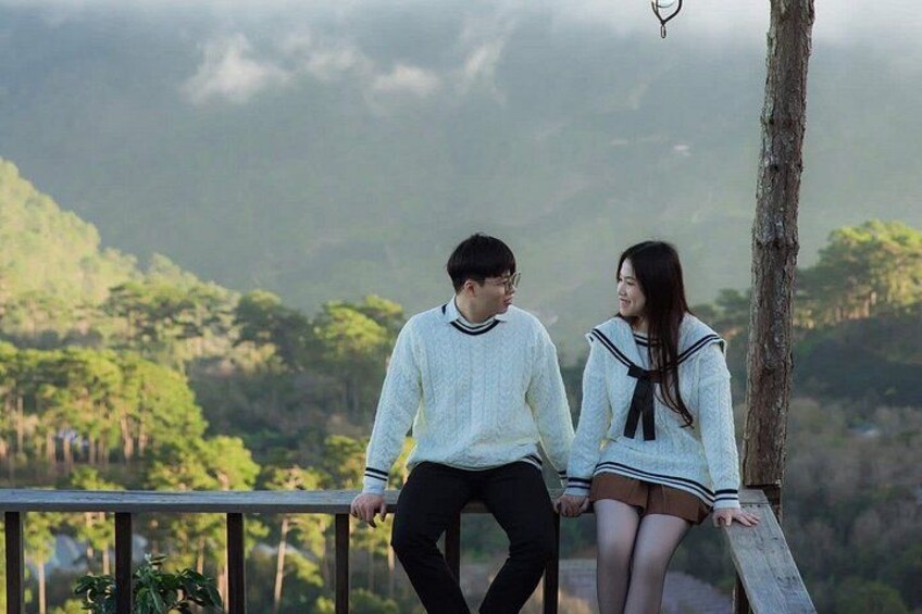 Two people sitting on a wooden bench overlooking a forested landscape. 3