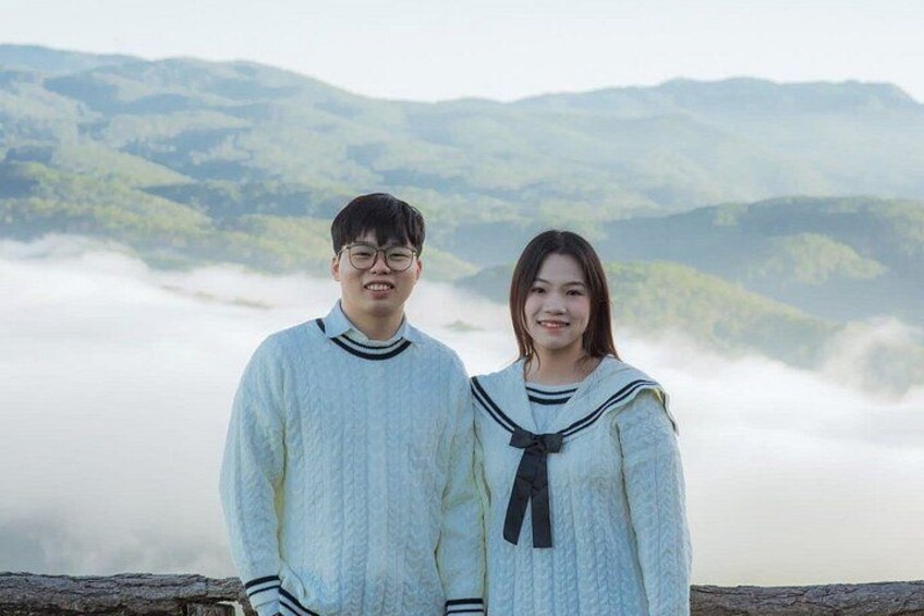 Two people standing in front of a mountainous landscape with fog. 2