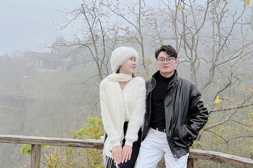 A couple standing on a wooden bridge with bare trees and a foggy background. 4