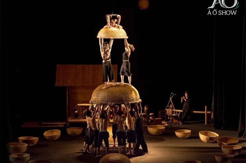 A performance with people balancing on large baskets, with a stage and audience in the background. 1