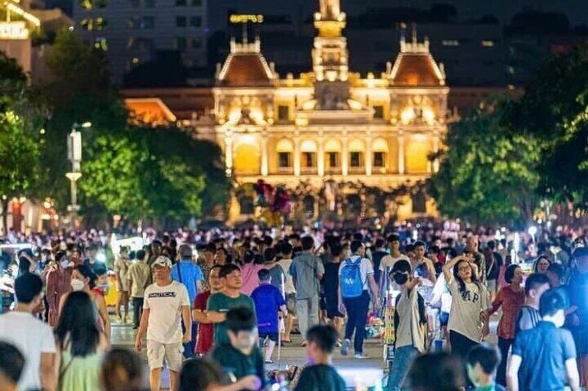 A crowded street with people walking towards a brightly lit historic building. 2