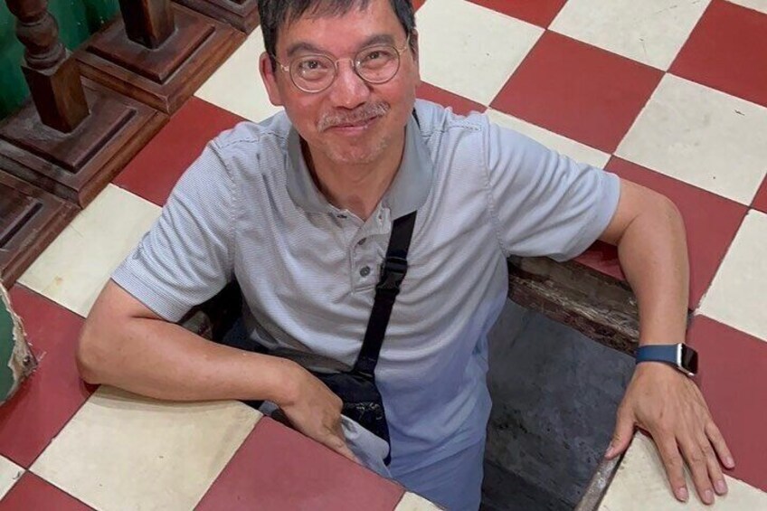 A man sitting on a checkered floor with a wooden chair in the background. 3