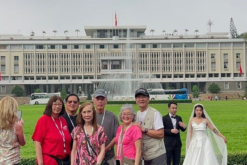 A group of people in front of a building with a fountain, a bus, and a flag. 2