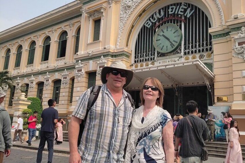 A man and a woman standing in front of a building with ornate architecture and a clock. 3