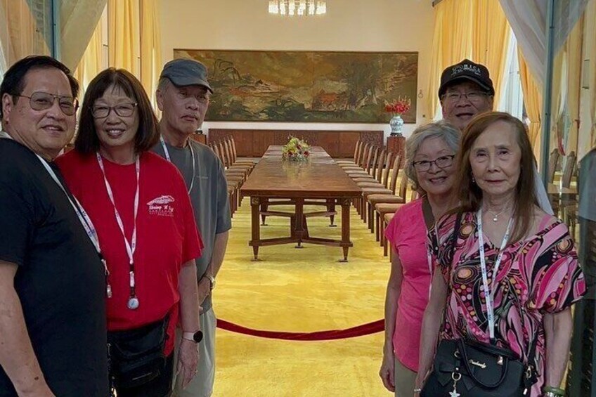 A group of people standing in a formal dining room with a long table and chairs. 5