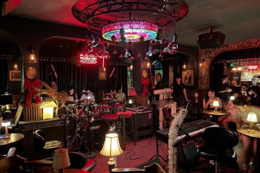 A dimly lit jazz club with a band performing, tables with patrons, and a vibrant red neon sign. 5