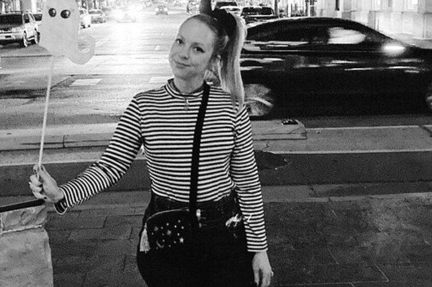 A person holding a balloon with a face design, standing on a sidewalk with a street and cars in the background. 2