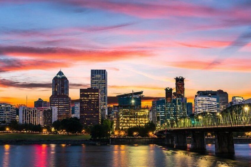 A city skyline at dusk with illuminated buildings, a bridge, and a river reflecting the lights. 3