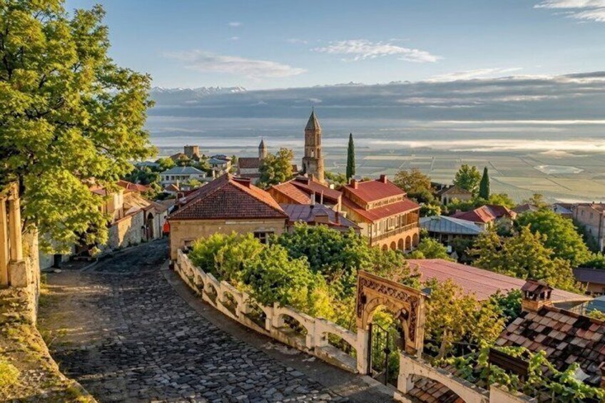 A historic town with cobblestone streets, a prominent church, and a mountain range in the background. 3