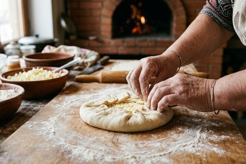 Hands shaping dough on a wooden surface with flour scattered around, bowls of ingredients, and a brick oven in the background. 3