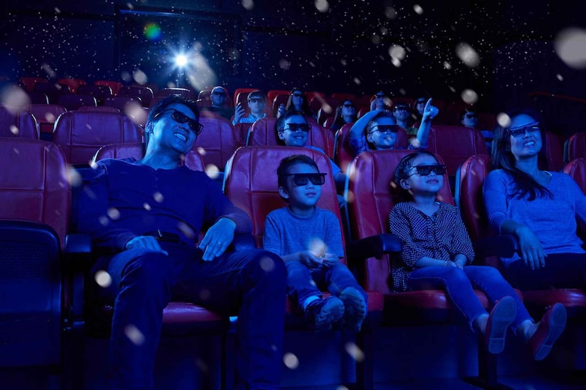 People in a movie theater with red seats and a dark screen. 4