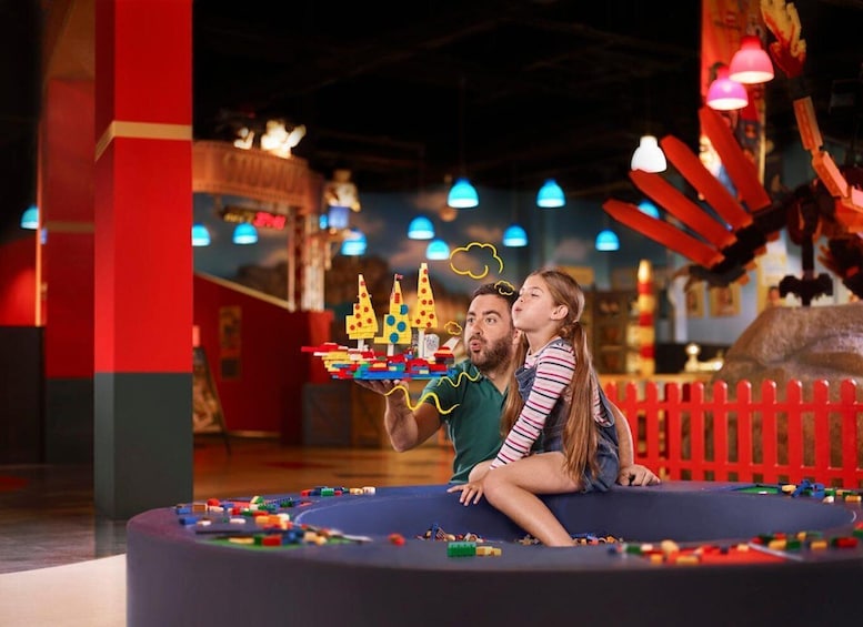 A child and an adult playing with colorful building blocks in a play area with a red fence and hanging lights. 3