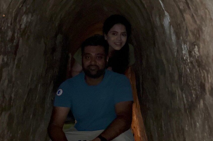 A person in a blue shirt and white pants inside a narrow, dimly lit tunnel with rough, textured walls. 4