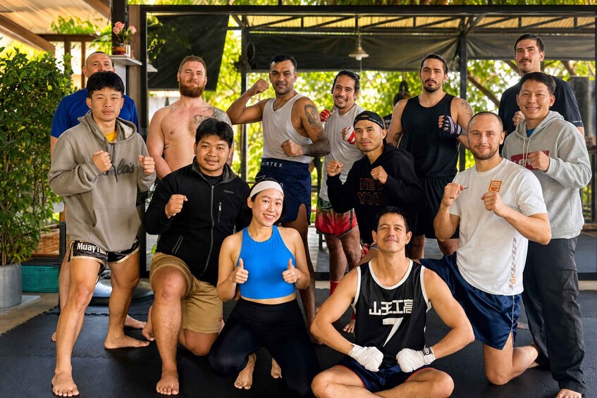 A group of people in a covered outdoor area with greenery in the background. 3