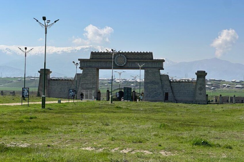 A stone archway with a clock, surrounded by a grassy field and mountains in the background. 5