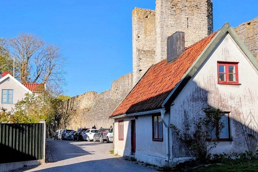 A white house with a red roof, a stone tower, and parked cars along a cobblestone street. 2