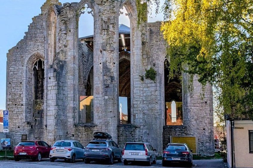 A historic stone structure with arches, parked cars, and a tree with yellow leaves. 3